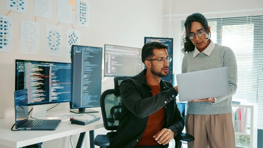 Image of Two Hispanic programmers reviewing code on a laptop in a modern office