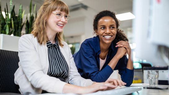 Two people smiling working on computer.