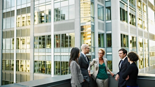 Boosting Trade and Collaboration Across the Commonwealth - Group of coworkers standing in discussion on deck of office buildings in background
