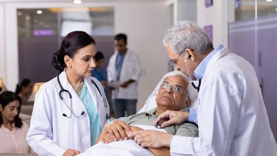 Doctors checking heartbeat of patient using stethoscope lying on hospital bed.