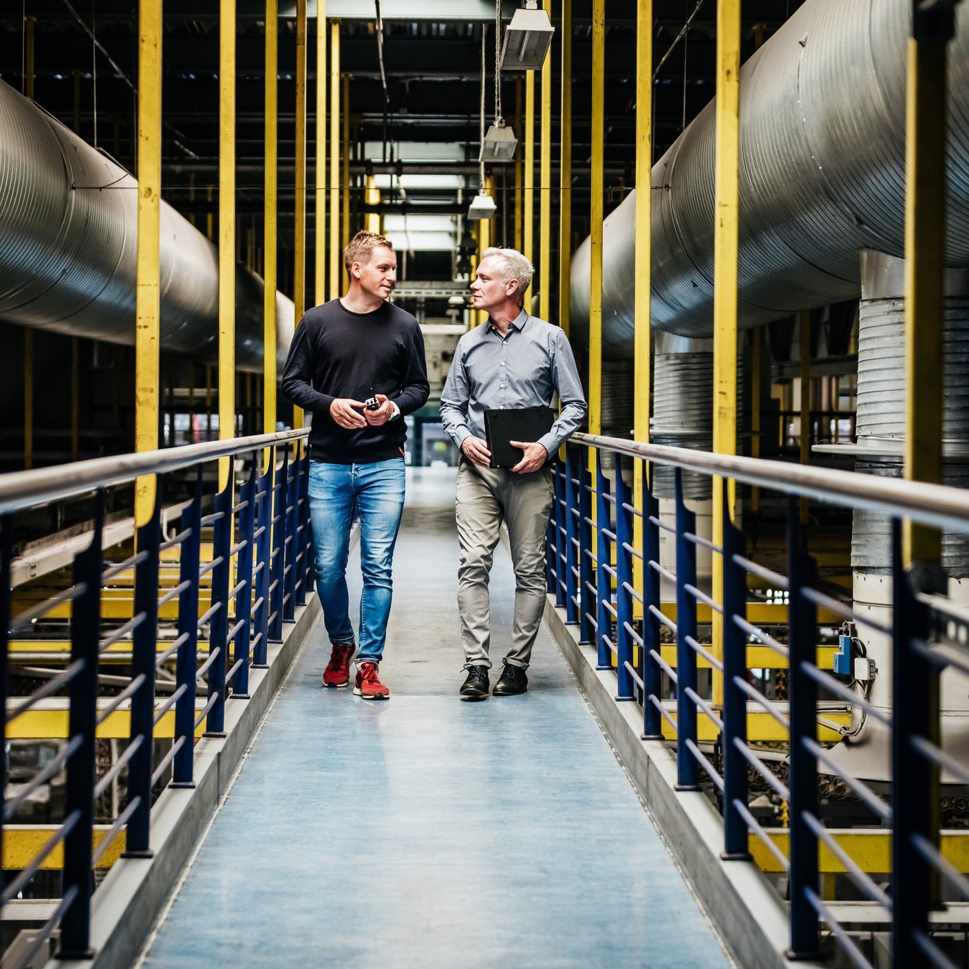A large printing factory with machinery and two engineers on a walkway together.