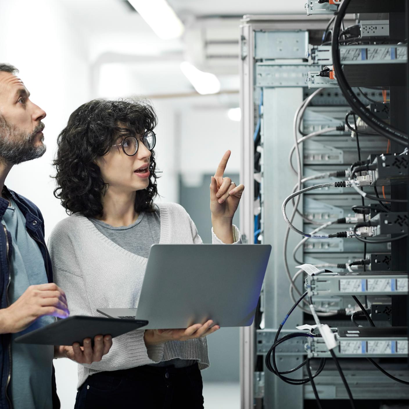 Female technician guiding male about cables.