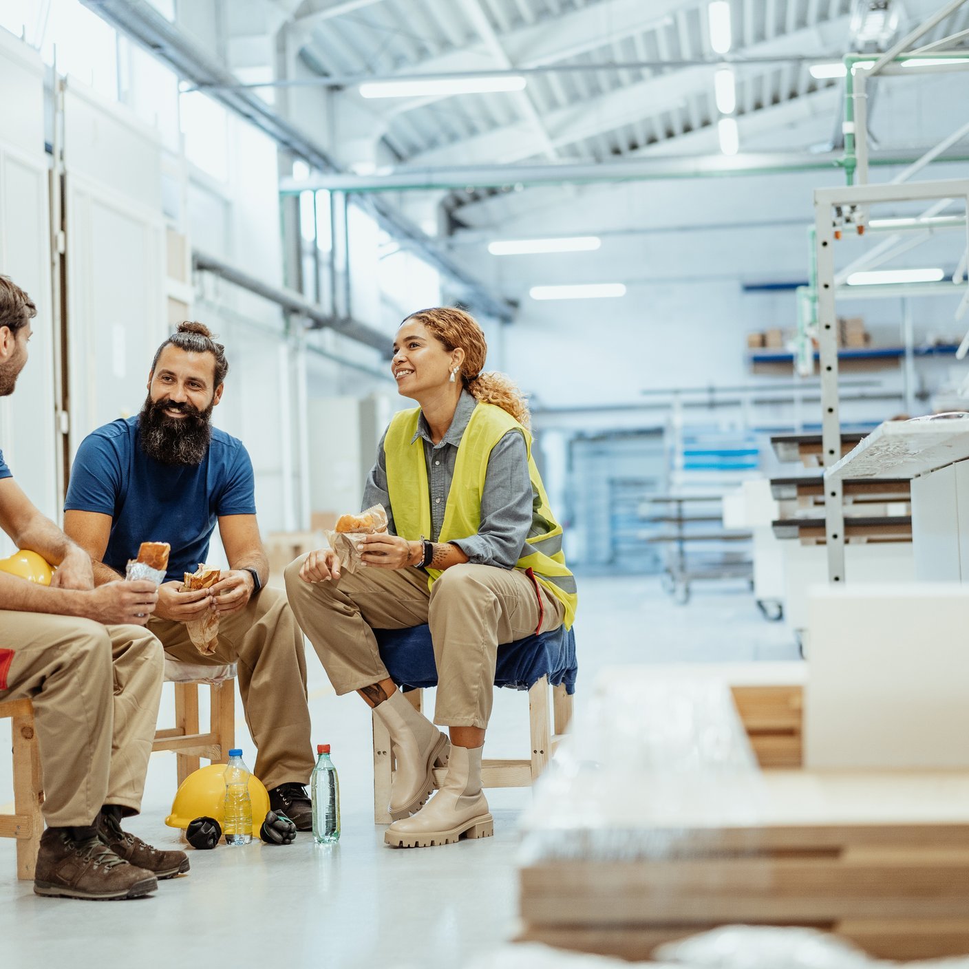 Engineers, architects and blue collar workers in protective clothing working in factory with modern machinery. Sitting for lunch and having a chat.
