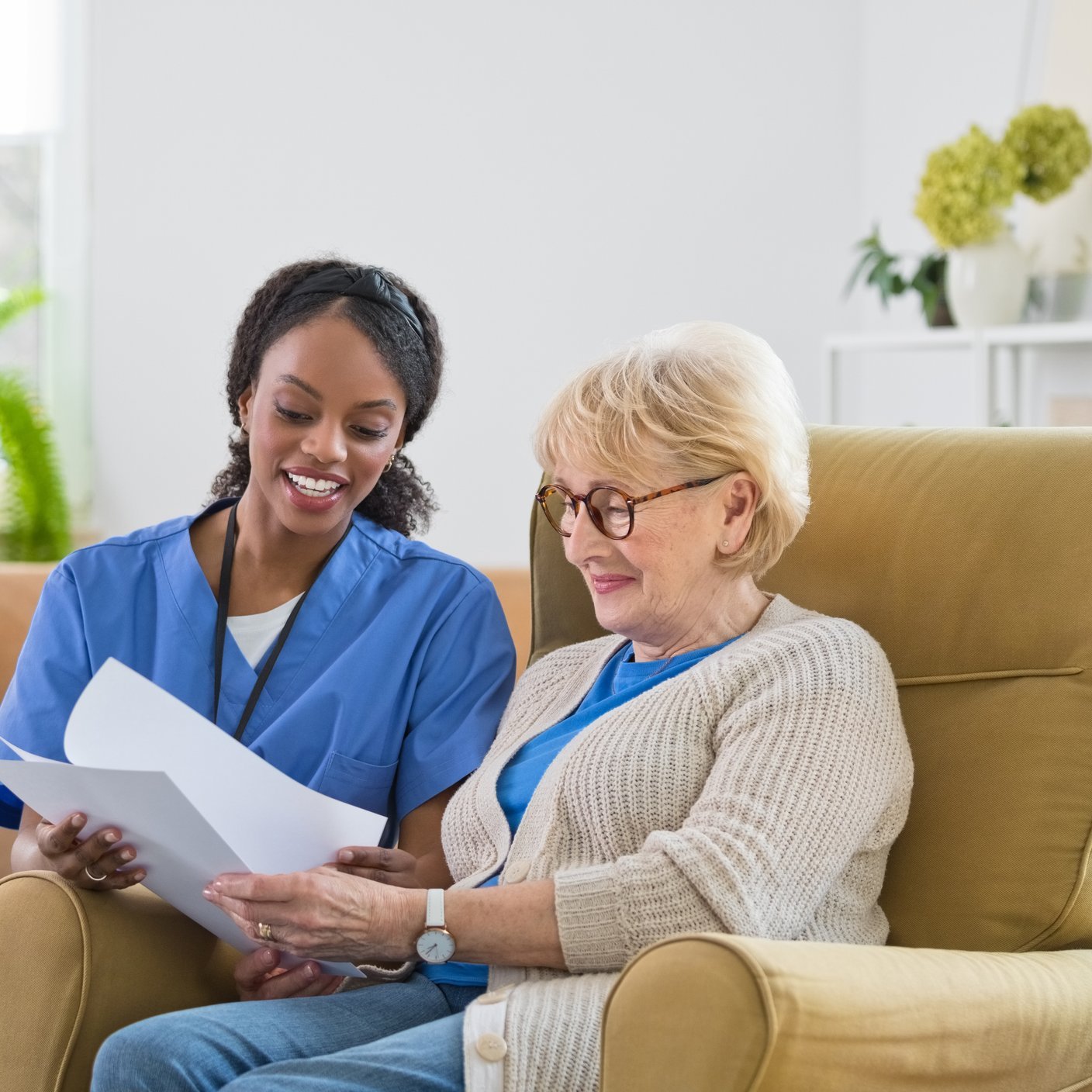 Female home caregiver supporting senior woman in her house, reviewing documents together.