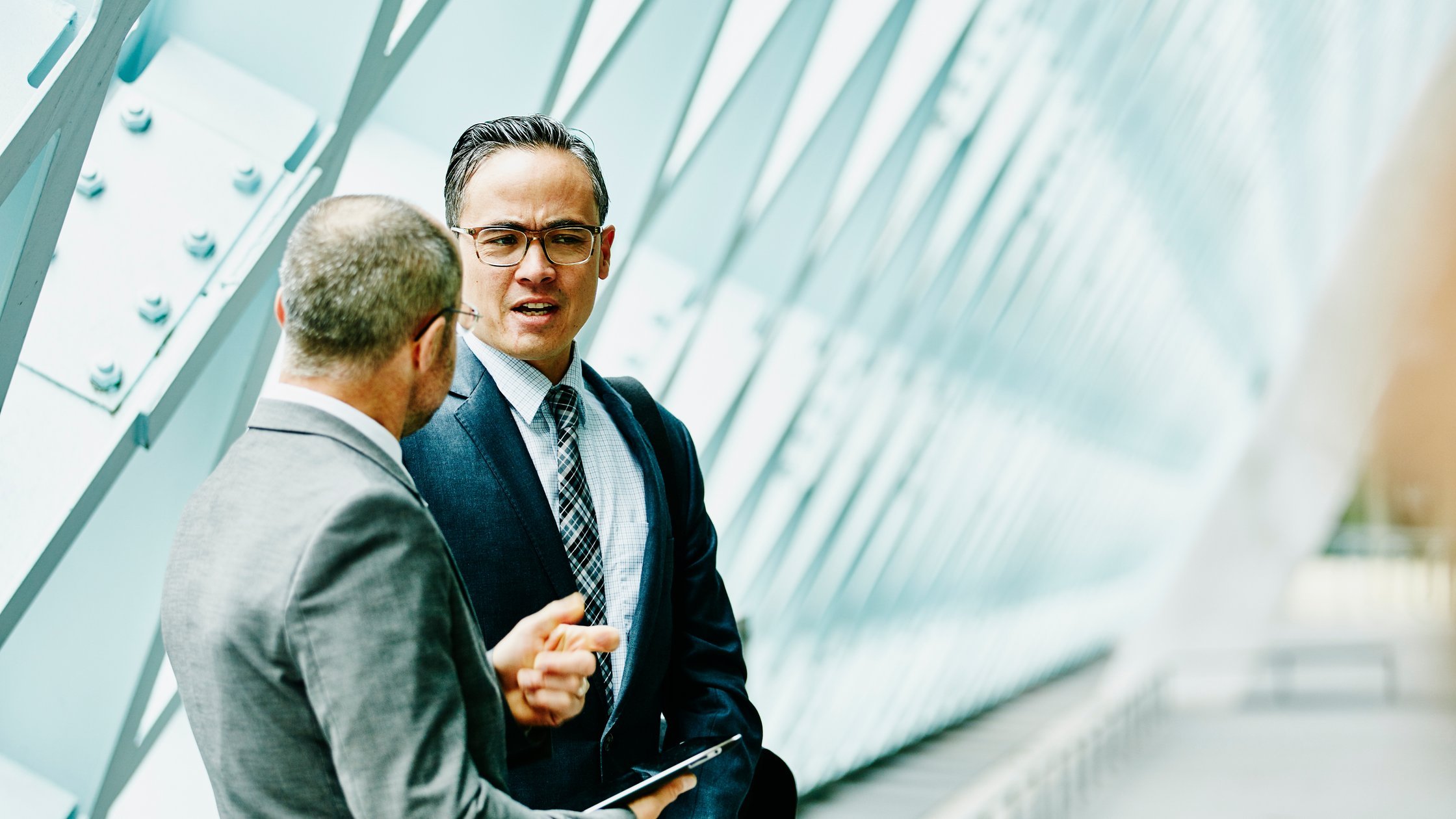 Two businessmen discussing data on digital tablet in informal meeting in building corridor