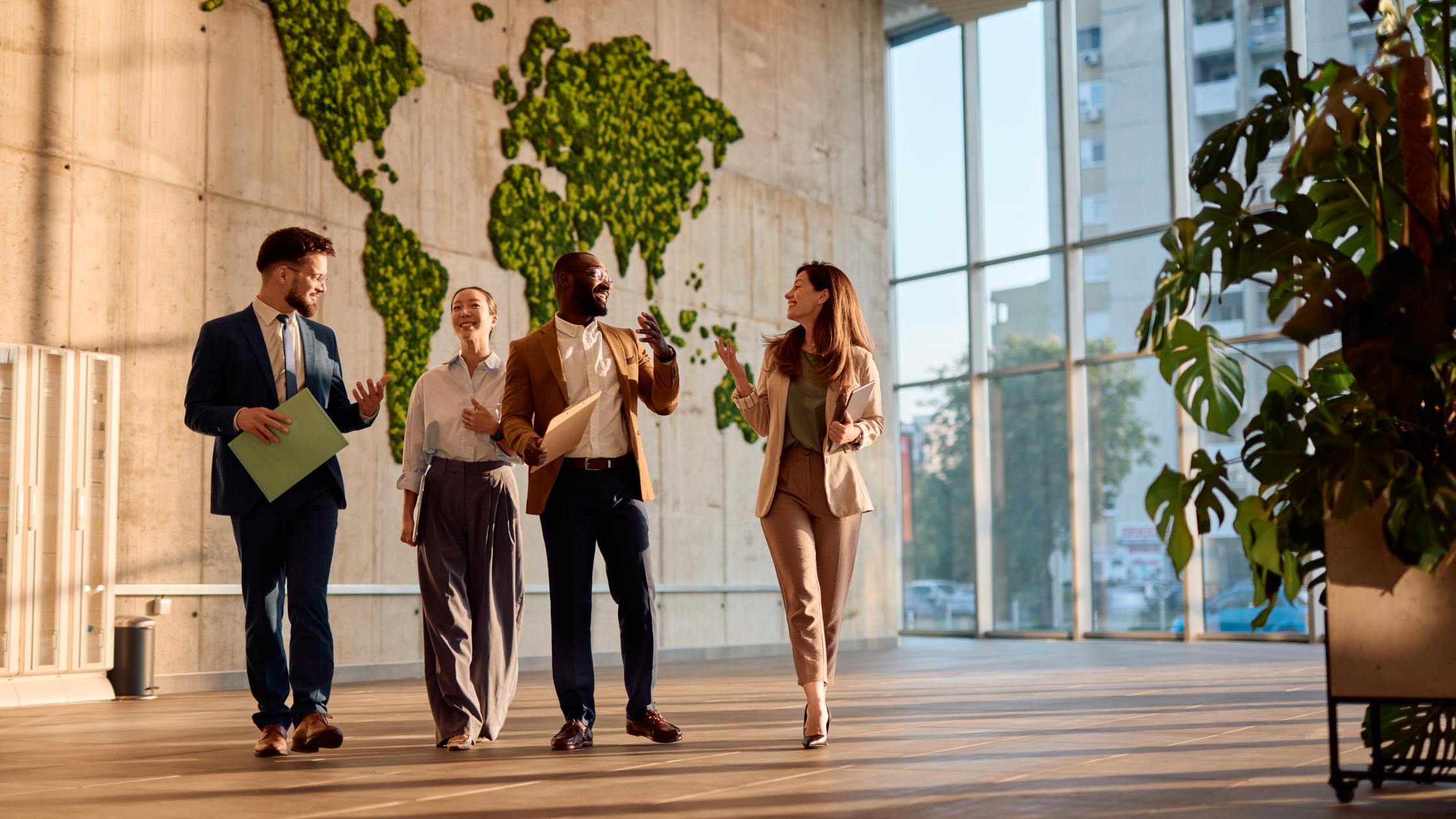 Four businesspeople walking and talking in a modern office with a lush moss wall.